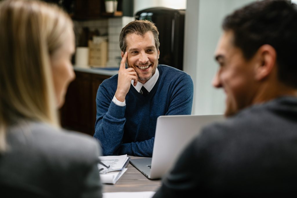 Happy financial advisor talking to a couple while having a meeting at their home.